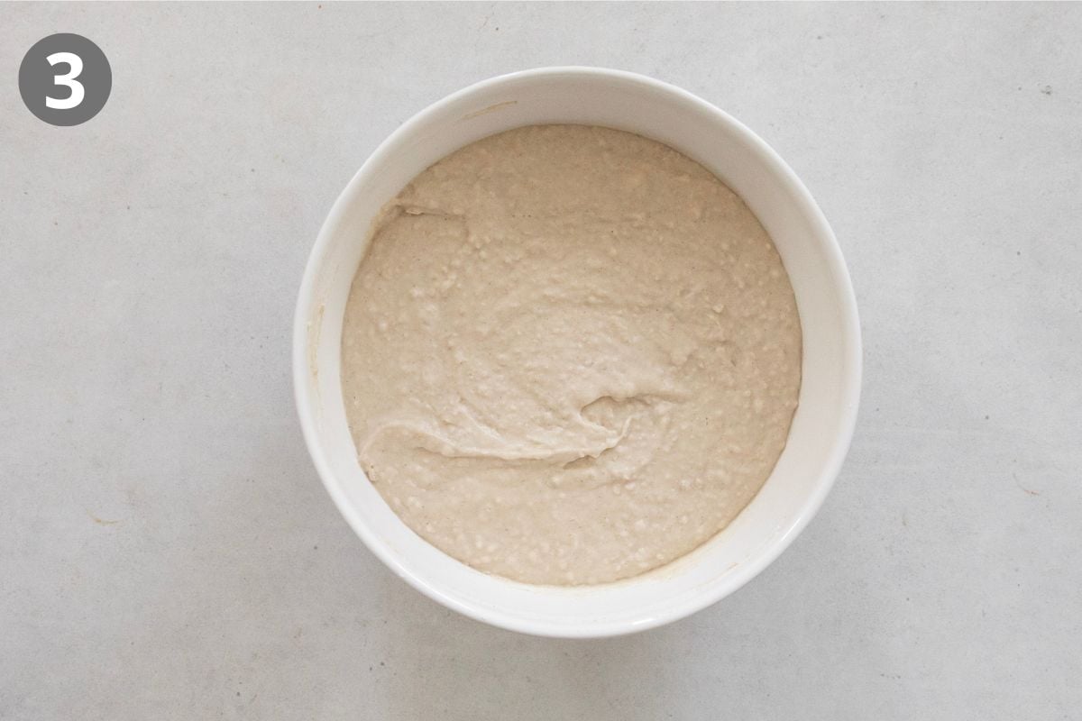 A white bowl filled with thick, pale batter sits on a light surface. A gray circle in the top left corner contains the number 3.