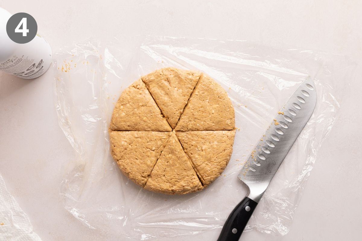 A round disk of dough on plastic wrap is cut into six wedges with a large knife beside it. The number 4 is in the top left corner.