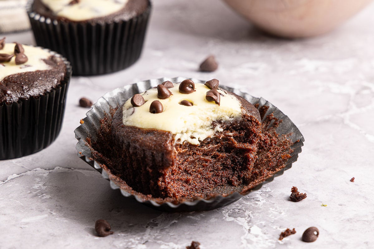 A chocolate black bottom cupcake with a white cream cheese center and chocolate chips, with a large bite taken out of it.