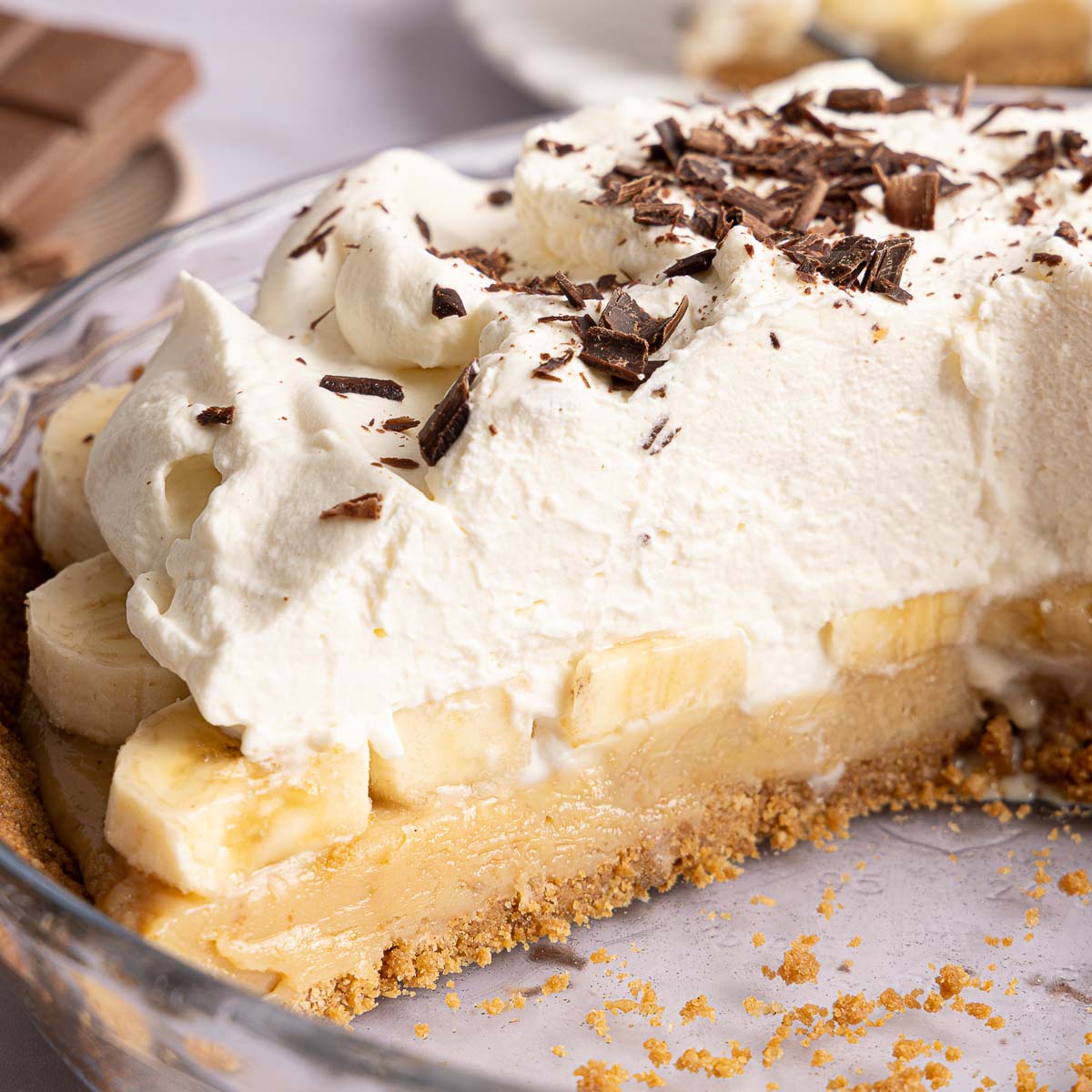 A slice of banoffee pie in a glass dish, topped with whipped cream and chocolate shavings.