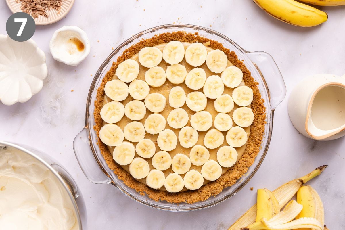 A glass pie dish filled with caramel topped with sliced bananas in a graham cracker crust.