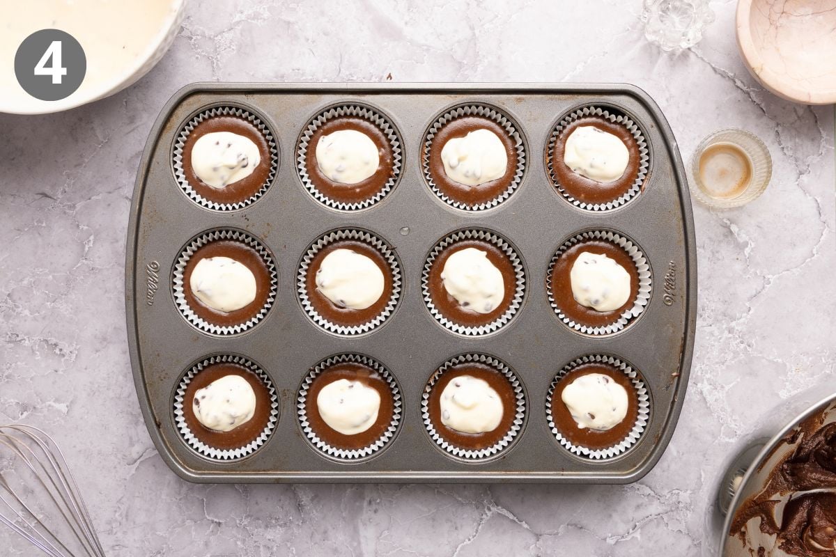 A muffin tin filled with twelve chocolate cupcakes, each topped with a dollop of cream cheese filling.
