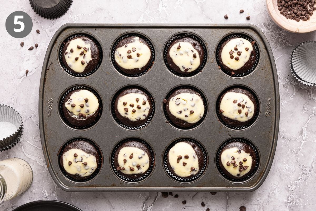 Twelve chocolate black bottom cupcakes with dollops of cream cheese and chocolate chips in a baking pan.
