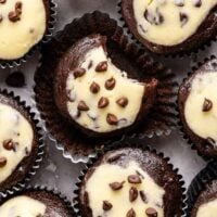 Several chocolate cupcakes with cheesecake centers and chocolate chips, one with a bite taken out of it.