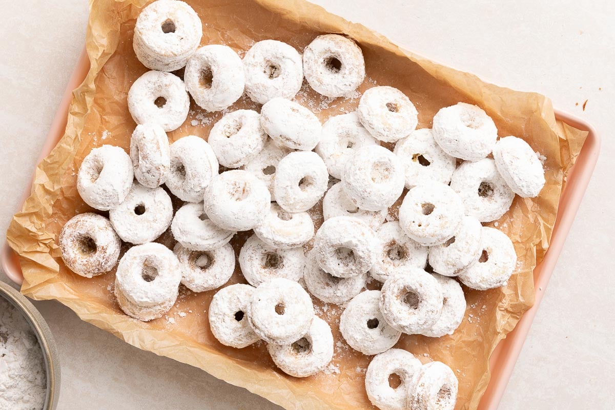 A tray lined with parchment paper filled with mini powdered sugar-coated donuts.
